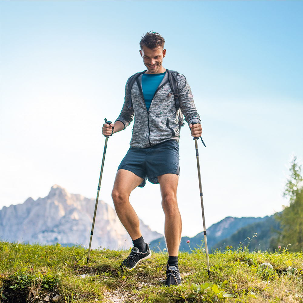 Een lachende man wandelt pijnvrij met wandelstokken in de bergen.