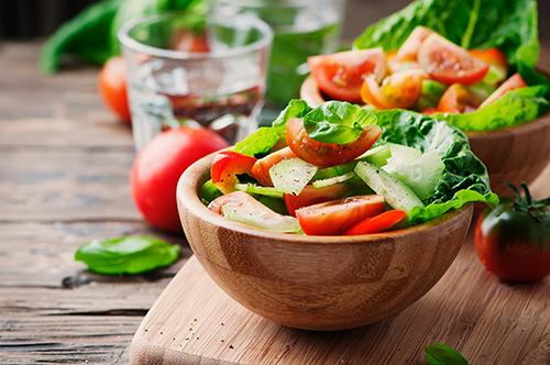 Twee houten schalen met gezond eten op een houten plank naast een glas water.
