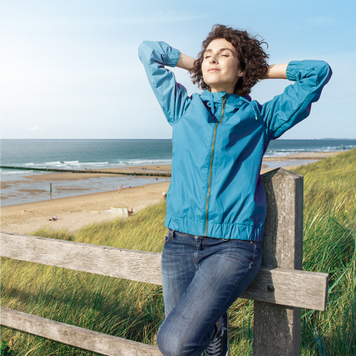 Een vrouw staat ontspannen en vrij van rugpijn op het strand en geniet met gesloten ogen van de zon.