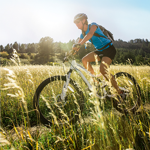 Een man die vrij is van sportblessures rijdt op de fiets op een veldweg onder de zon.
