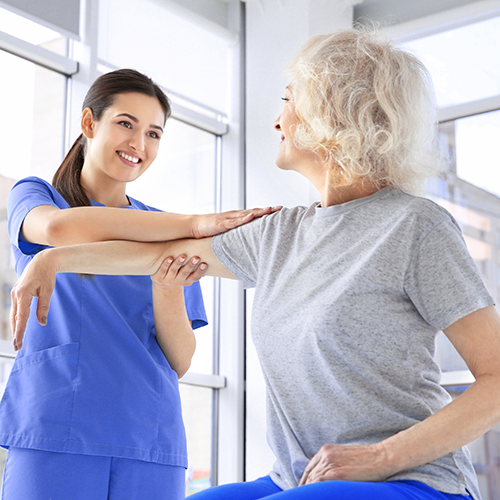 Een fysiotherapeute helpt een oude vrouw bij een rekoefening voor de armen.