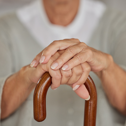 Handen van een oudere vrouw die een wandelhulp voor artrosepatiënten vasthoudt.