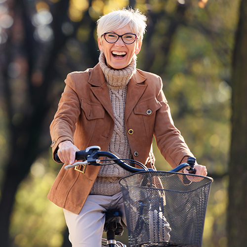 Een oudere, gezonde vrouw fiets pijnvrij en lachend in het bos.