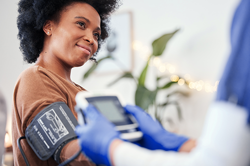 Een lachende vrouw laat als ambulant patiënt haar bloeddruk meten door een arts met een manchet rond de arm.