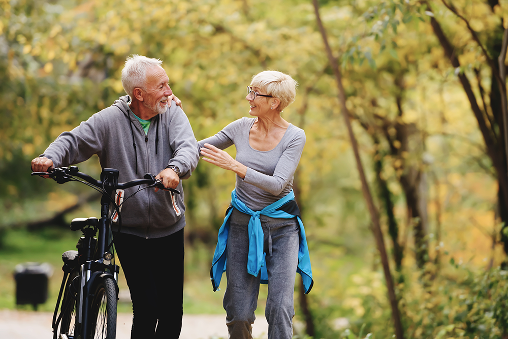 Ein älterer Mann und Frau sind draußen aktiv mit Fahrrad und zu Fuß ohne Schmerzen.