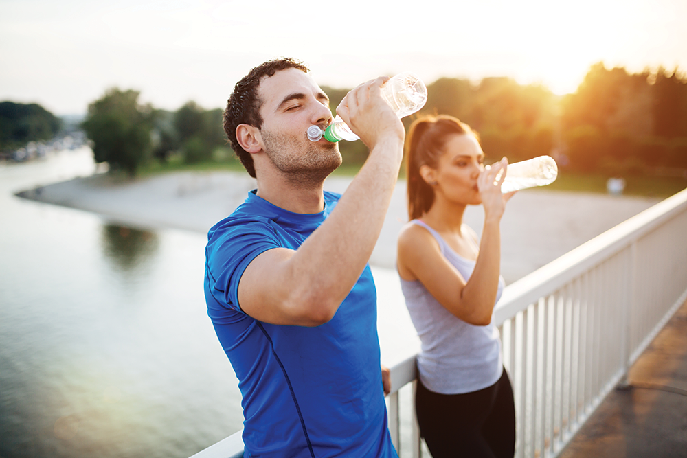 Een jonge man en vrouwen nemen pauze van een jogsessie en drinken een flesje water.