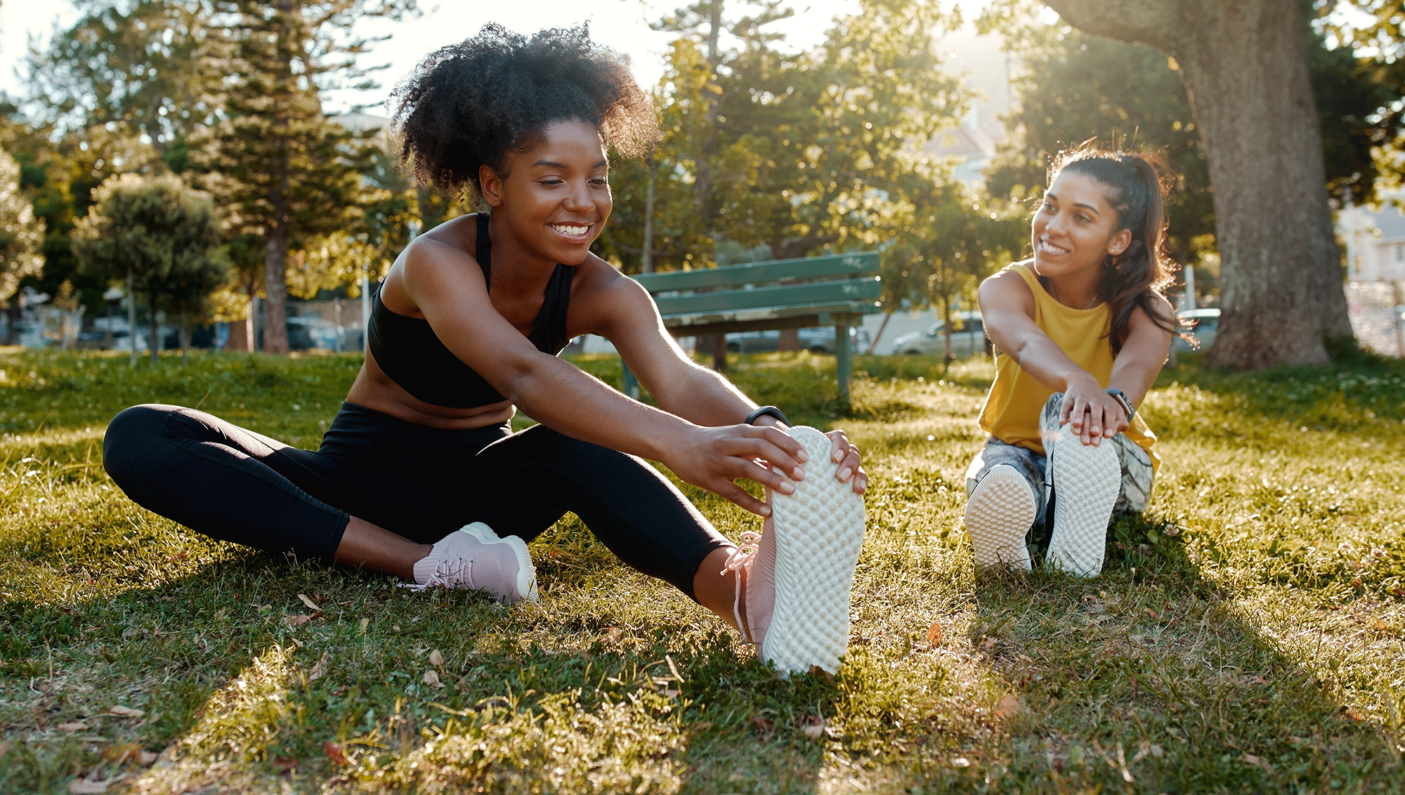 Twee jonge sportsters strekken hun enkels voor het sporten in het park