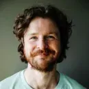 Smiling man with curly brown hair and beard wearing a light green shirt.
