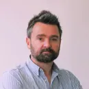 Portrait of a man with dark hair and beard wearing a light blue shirt against a plain background.