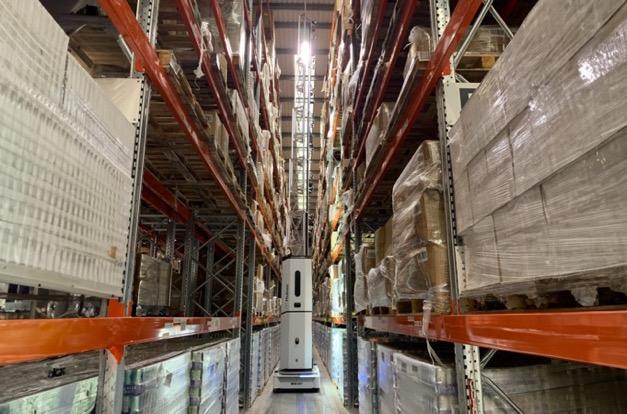 The Dexory robot with the tower extended in an aisle of a warehouse scanning pallets on a rack