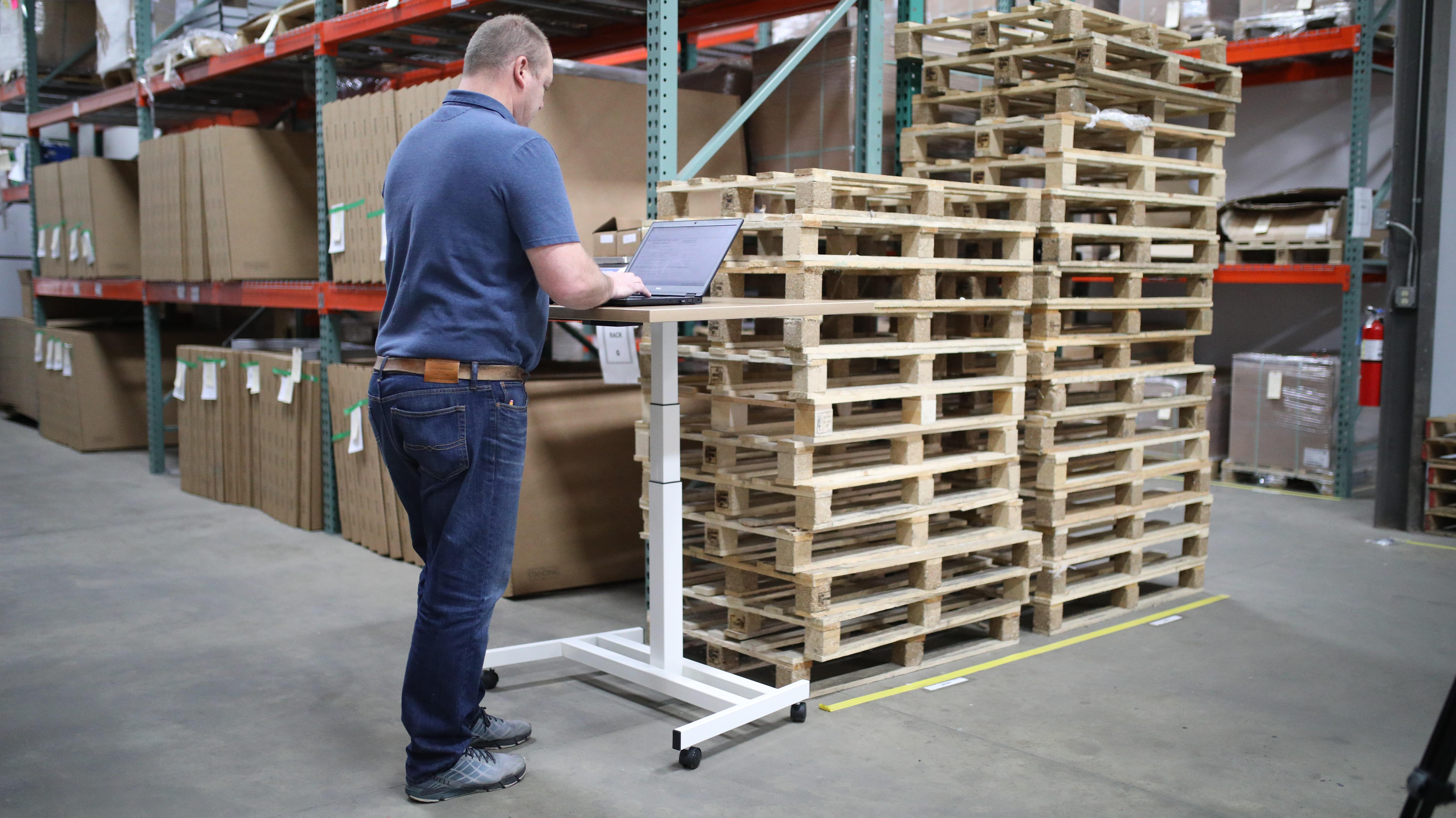 Man stood at a desk, on his computer, with a warehouse background behind him