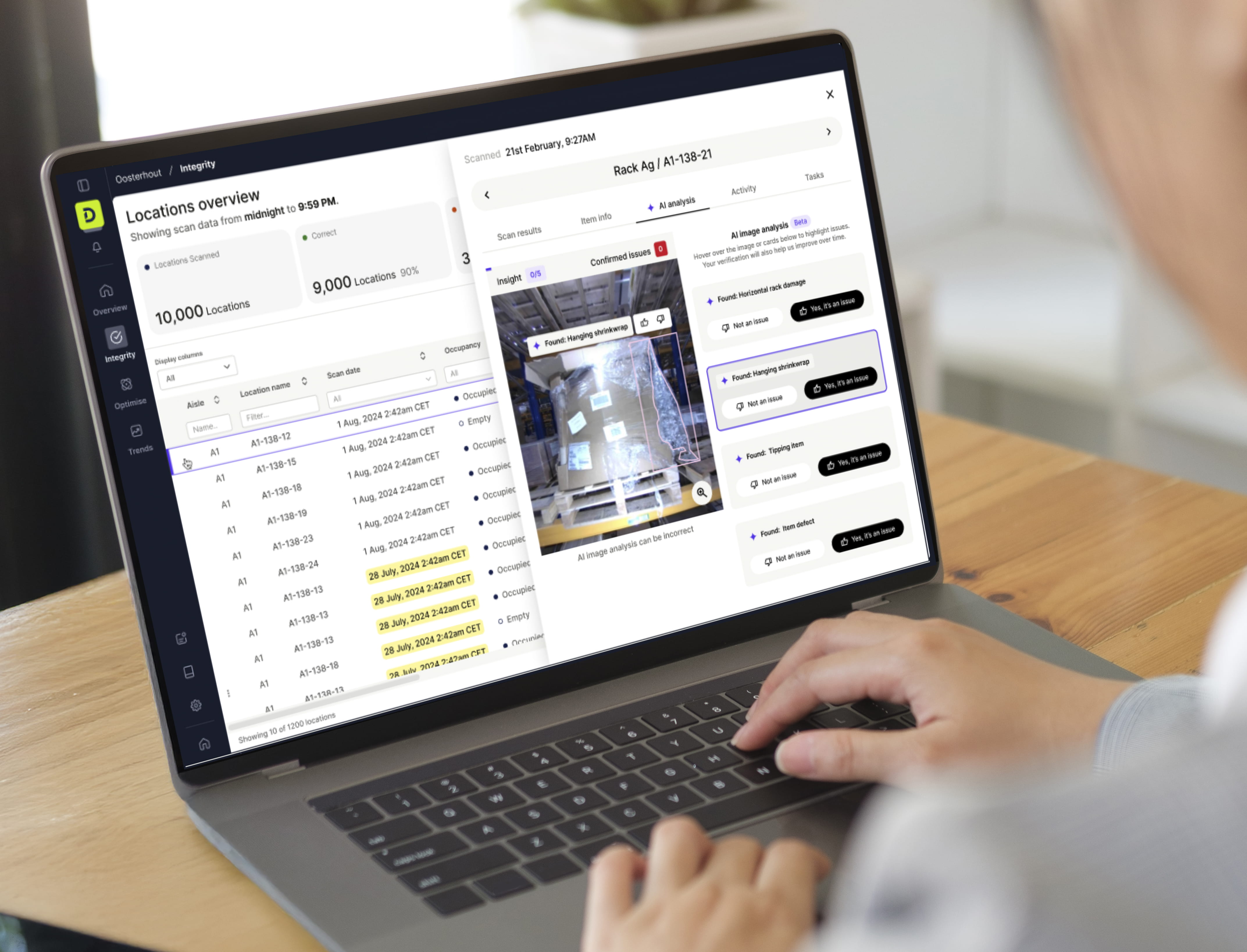 Warehouse manager reviewing DexoryView Integrity Storage Health platform on a laptop, showing AI-powered detection of rack damage, hanging shrinkwrap, tipping items and item defects across 10,000 scanned locations, enhanced by NVIDIA Cosmos foundation model integration for improved warehouse storage anomaly identification.
