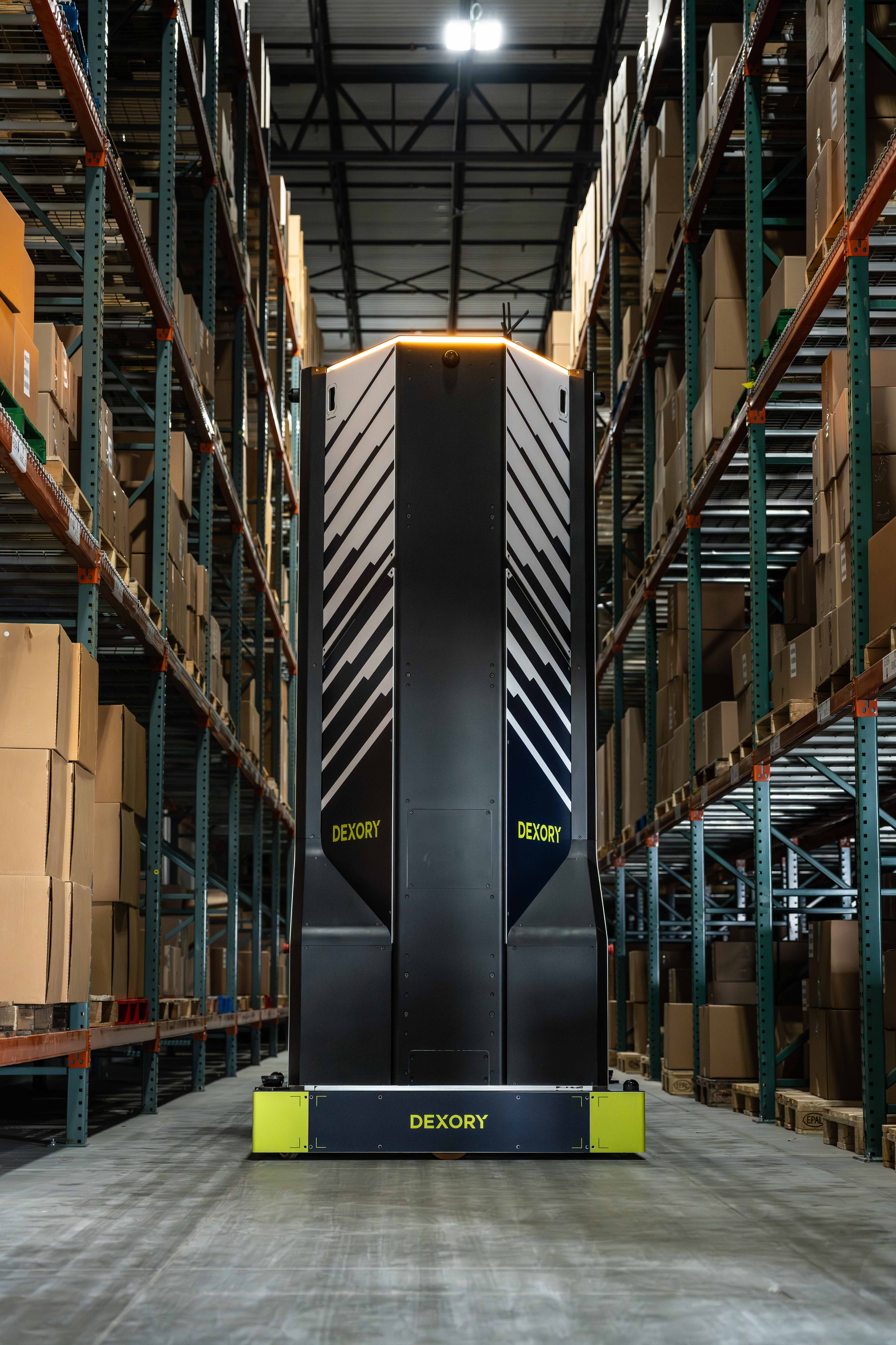 Dexory’s next generation autonomous warehouse robot navigating a densely stocked warehouse aisle, representing the deployment of physical AI with NVIDIA Halos safety platform to ensure safe 24/7 autonomous operation alongside people, forklifts and equipment in complex industrial environments.