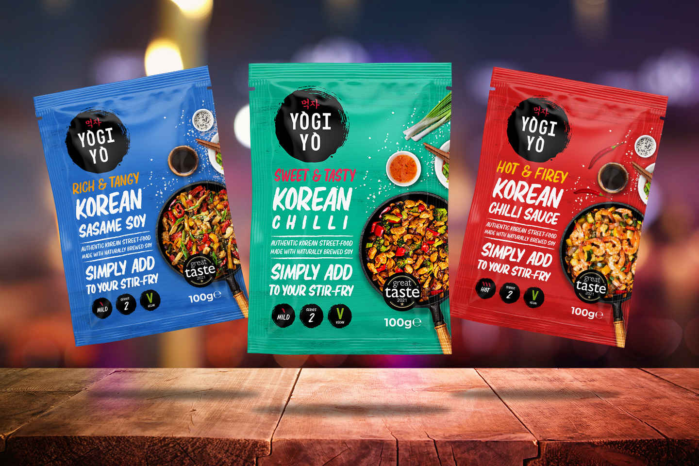 Three colorful packets of Yogi Yo Korean stir-fry sauces: blue Sesame Soy, green Sweet & Tasty Chilli, and red Hot & Firey Chilli Sauce, each serving 2 and labeled vegan.