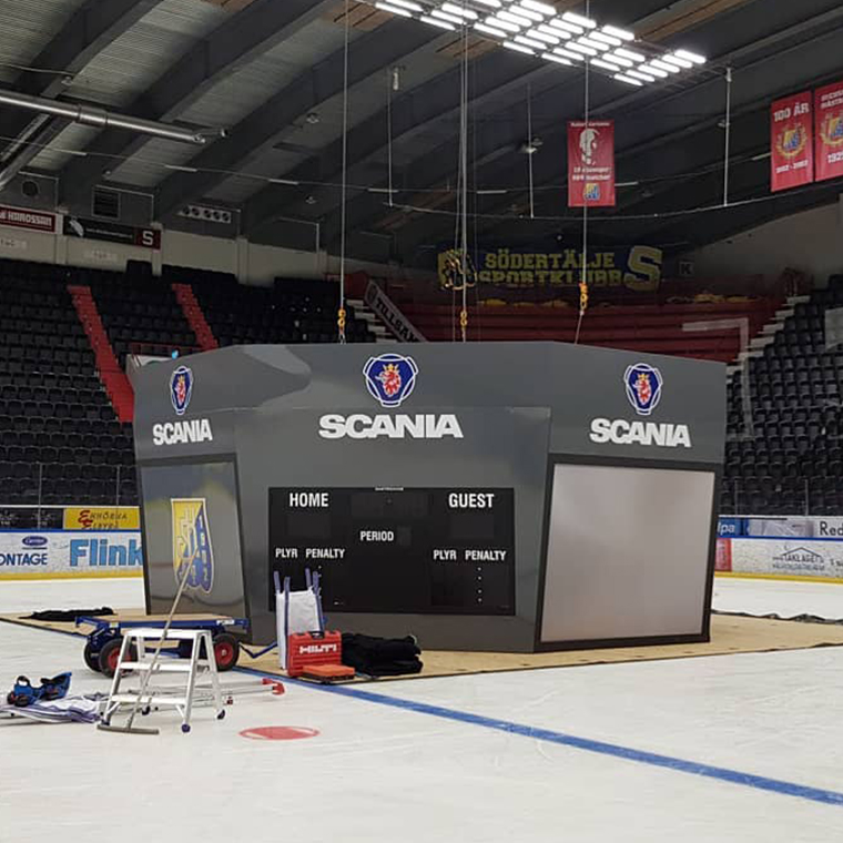 Large gray ice hockey scoreboard with Scania logos on an indoor ice rink under installation.