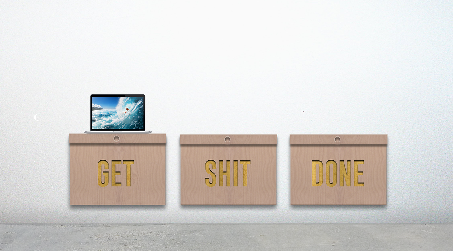 Three wooden boxes mounted on a white wall with gold text reading 'GET', 'SHIT', 'DONE', and a laptop showing a surfer on a wave placed on the left box.