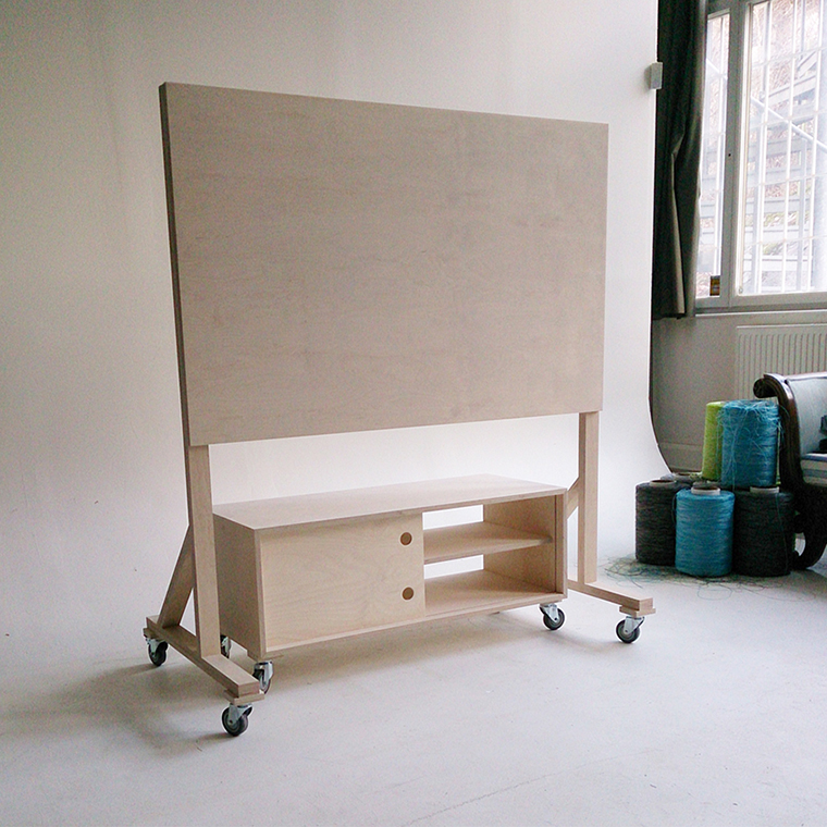 Minimalist light wood TV stand with a large vertical panel and open storage on caster wheels in a bright room.