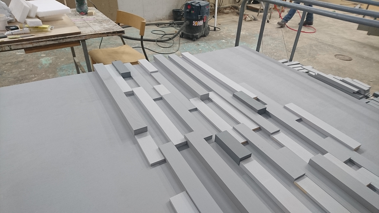 Multiple gray wooden planks of varying lengths arranged parallel on a gray table in a workshop.