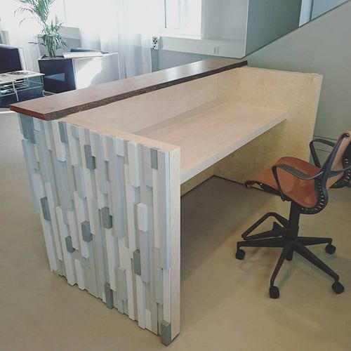 Modern office workspace with a light wood desk featuring a textured front panel and a brown swivel chair on a light floor.