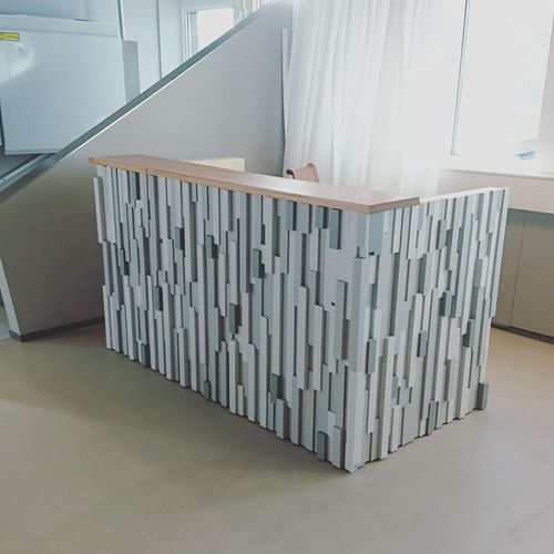 Modern reception desk with textured vertical gray panels and a wooden countertop in a bright room.