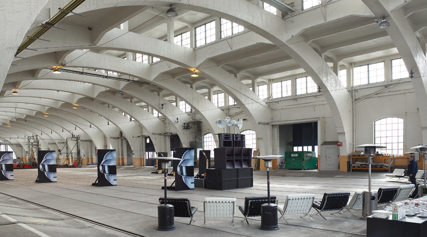 Large industrial hall with rows of Daft Punk helmet images, stacked speakers, and chairs arranged in a semi-circle.