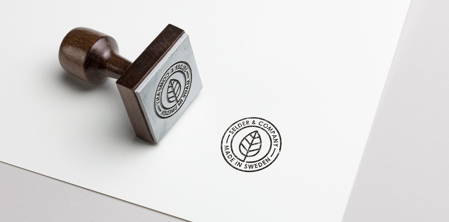 Wooden-handled rubber stamp and a stamped imprint reading 'Selder & Company Made in Sweden' with a leaf logo on white paper.