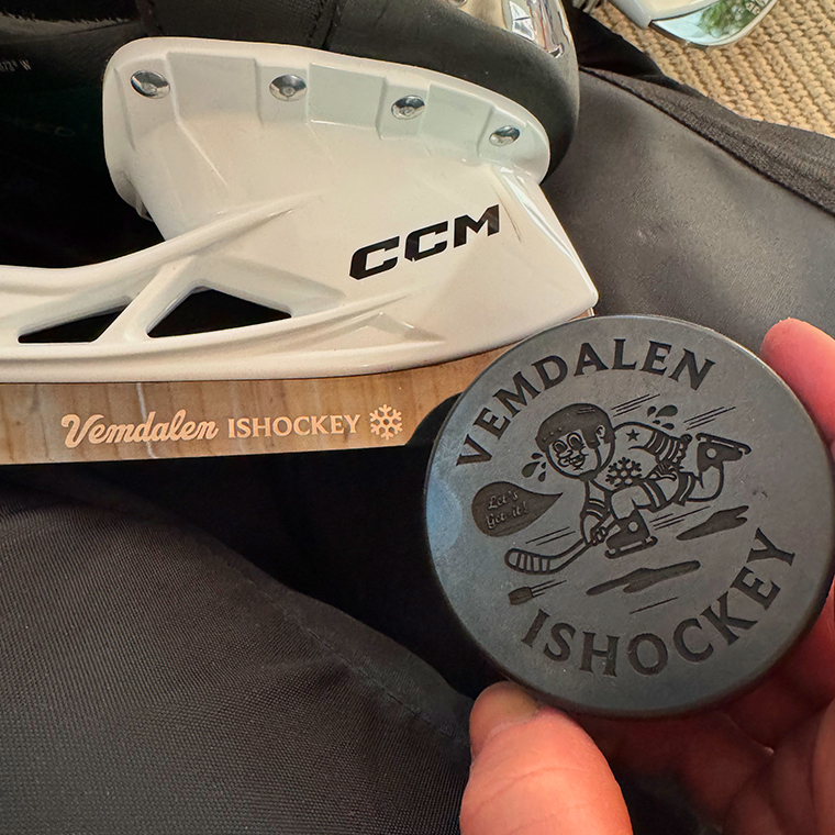 Close-up of a CCM ice skate blade with 'Vemdalen Ishockey' branding and a hand holding a hockey puck featuring a cartoon hockey player and the text 'Vemdalen Ishockey'.