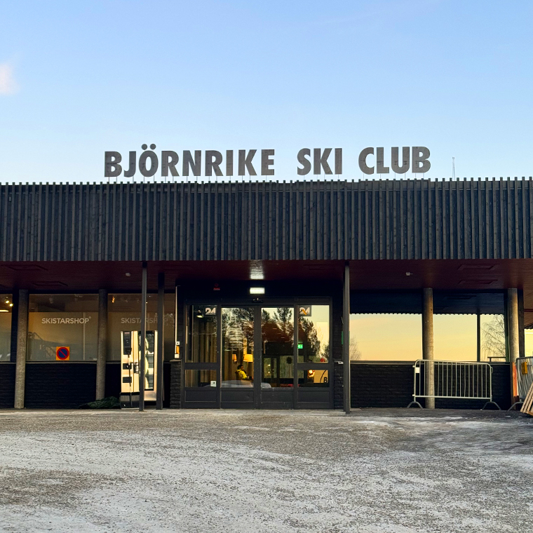 Entrance of Björnrike Ski Club building with large sign on roof at sunset.