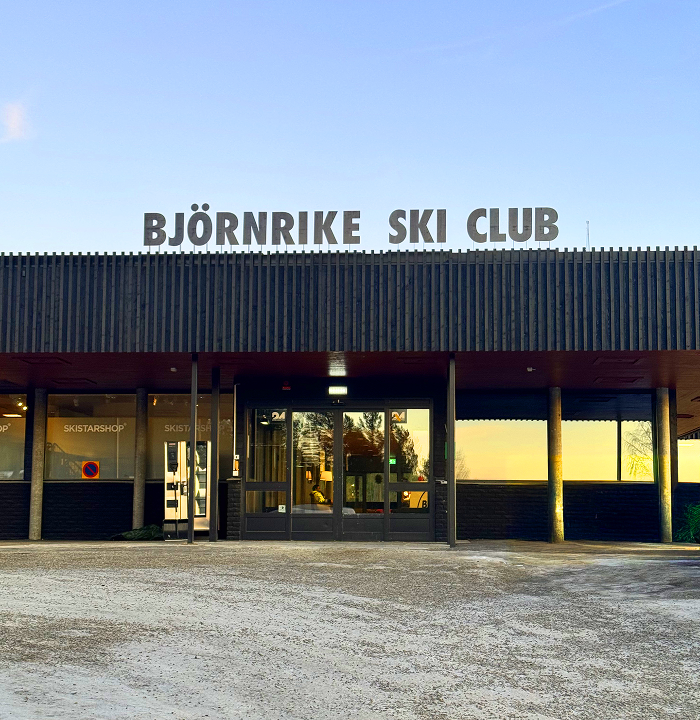 Entrance of Björnrike Ski Club building with large sign above the door and reflections in the windows.
