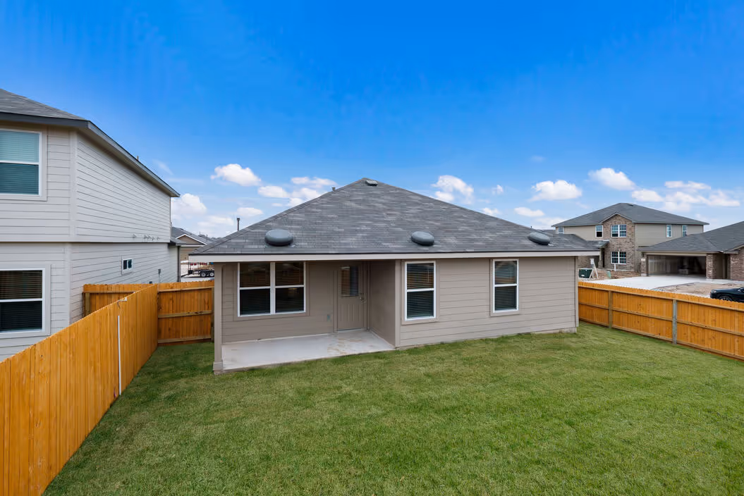 Spacious backyard with green grass and a concrete patio behind a single-story home, at Enclave at Medina in Von Ormy, TX.
