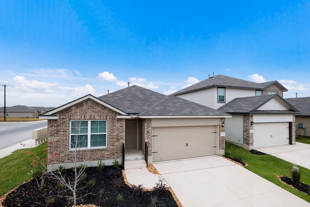 Front exterior of a newly built brick house with a beige garage and well-maintained landscaping at Enclave at Medina in Von Ormy, TX.
