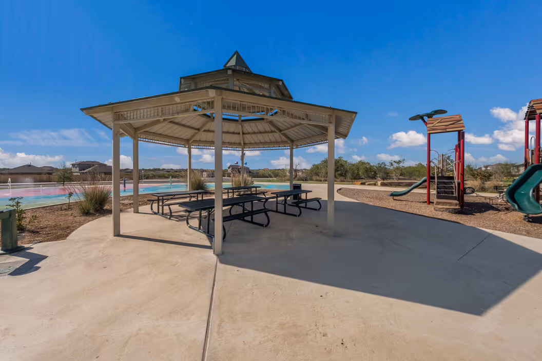 Community gazebo with picnic tables next to a playground and splash pad, offering outdoor recreation at Enclave at Medina in Von Ormy, TX.