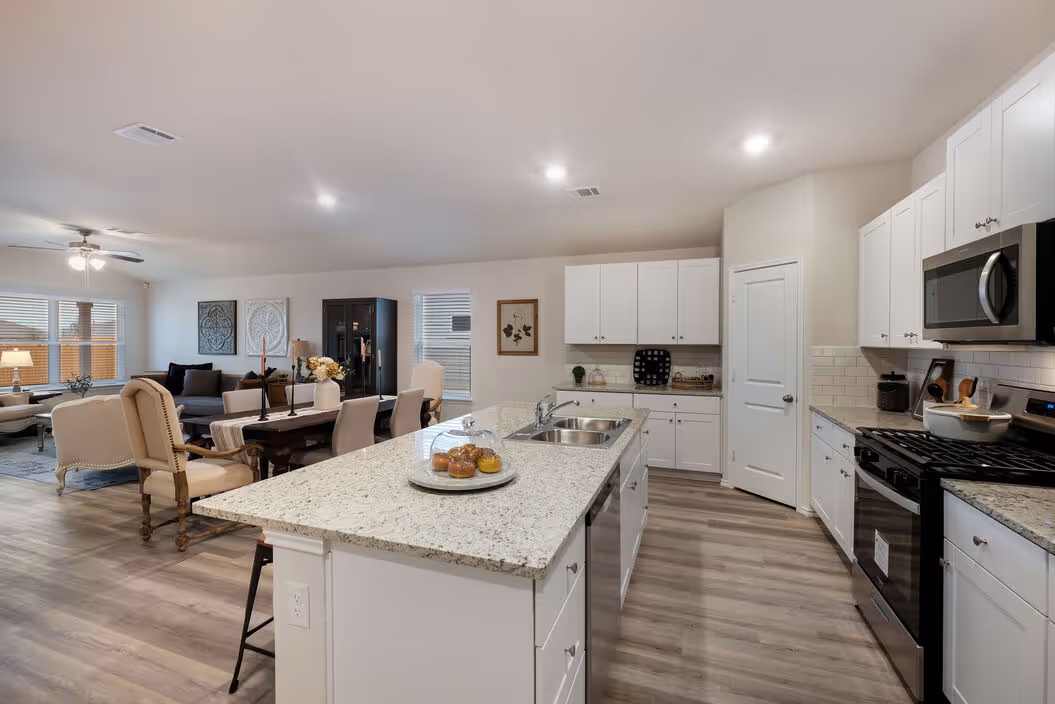 Open-concept kitchen and living area with white cabinets, a large island, and wood-look flooring, showcasing a home at Enclave at Medina in Von Ormy, TX.