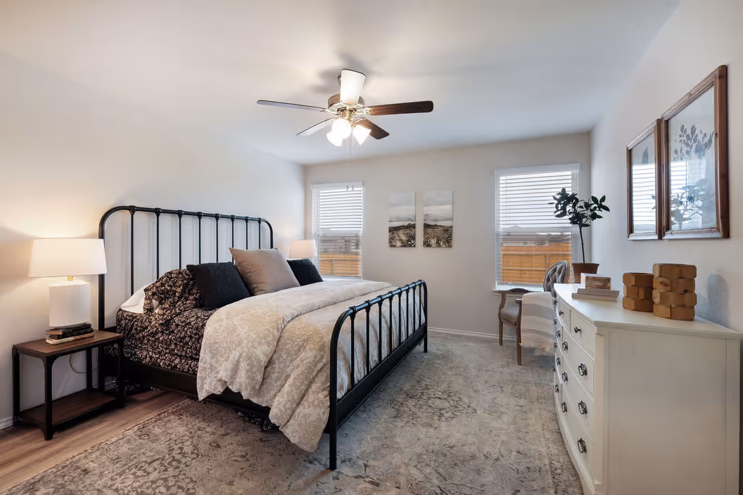 Spacious master bedroom with a large bed, ceiling fan, ample natural light, and a white dresser, in a home at Enclave at Medina in Von Ormy, TX.