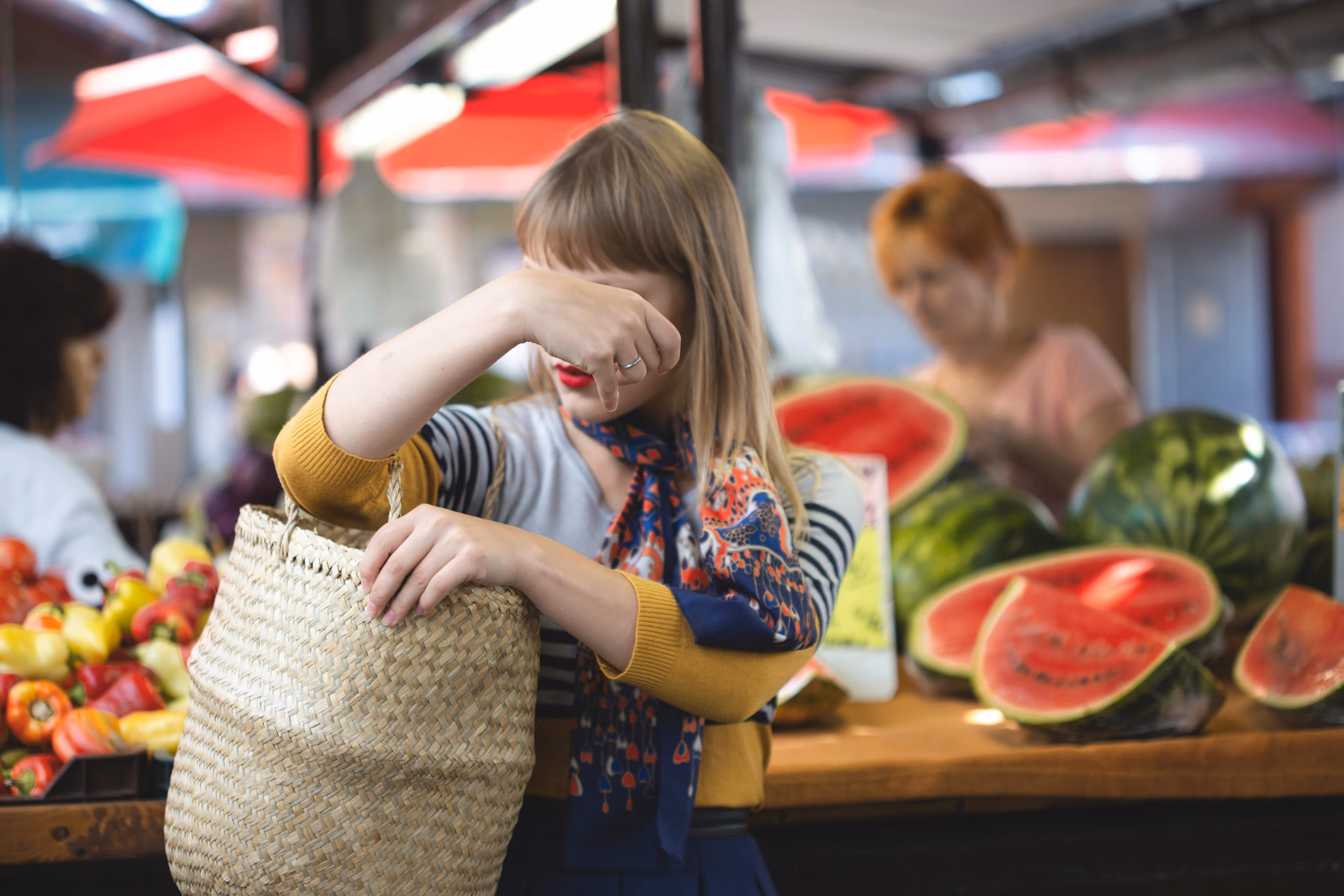 Woman holding a straw bag and shielding her eyes from the sun at an outdoor market with fresh produce, representing local attractions near Enclave at Medina in Von Ormy, TX.
