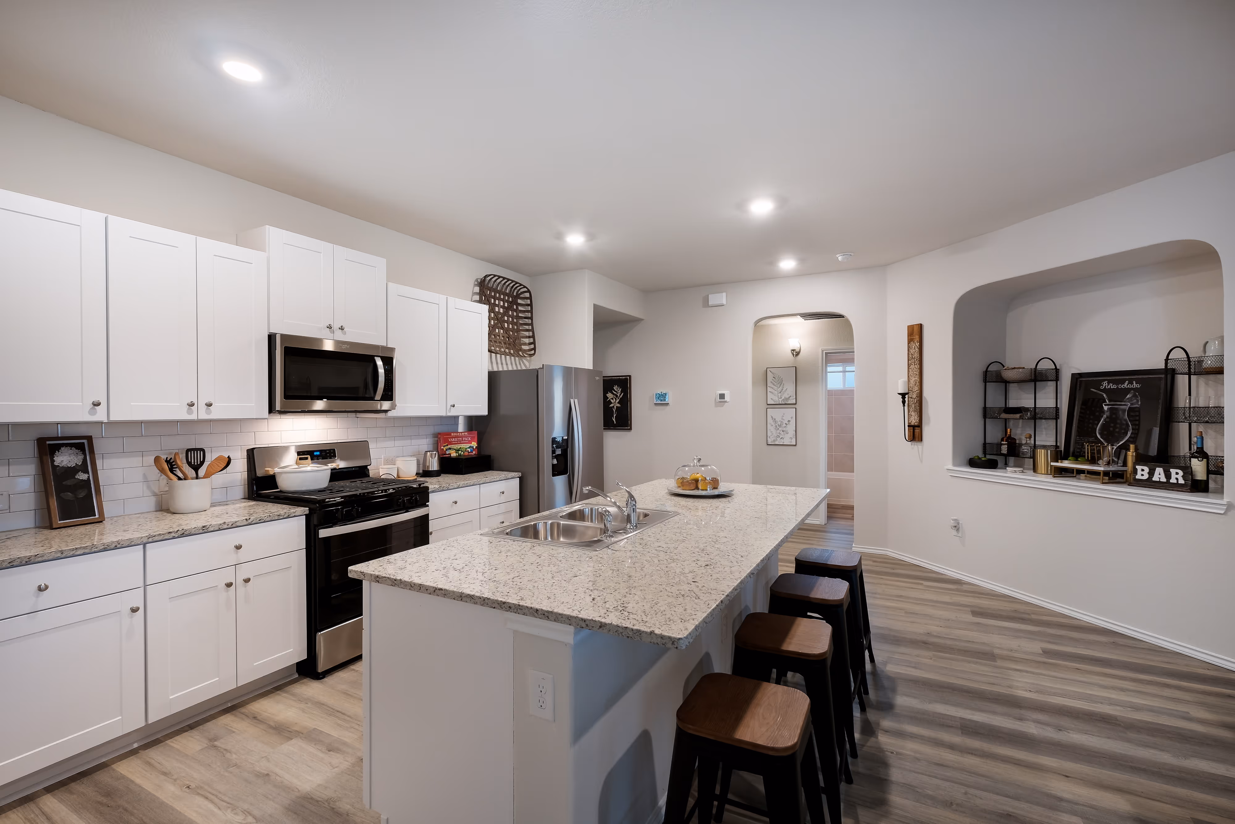 Modern kitchen with white cabinets, granite countertops, and a large island with bar seating, featuring a built-in bar nook, at Enclave at Medina in Von Ormy, TX.