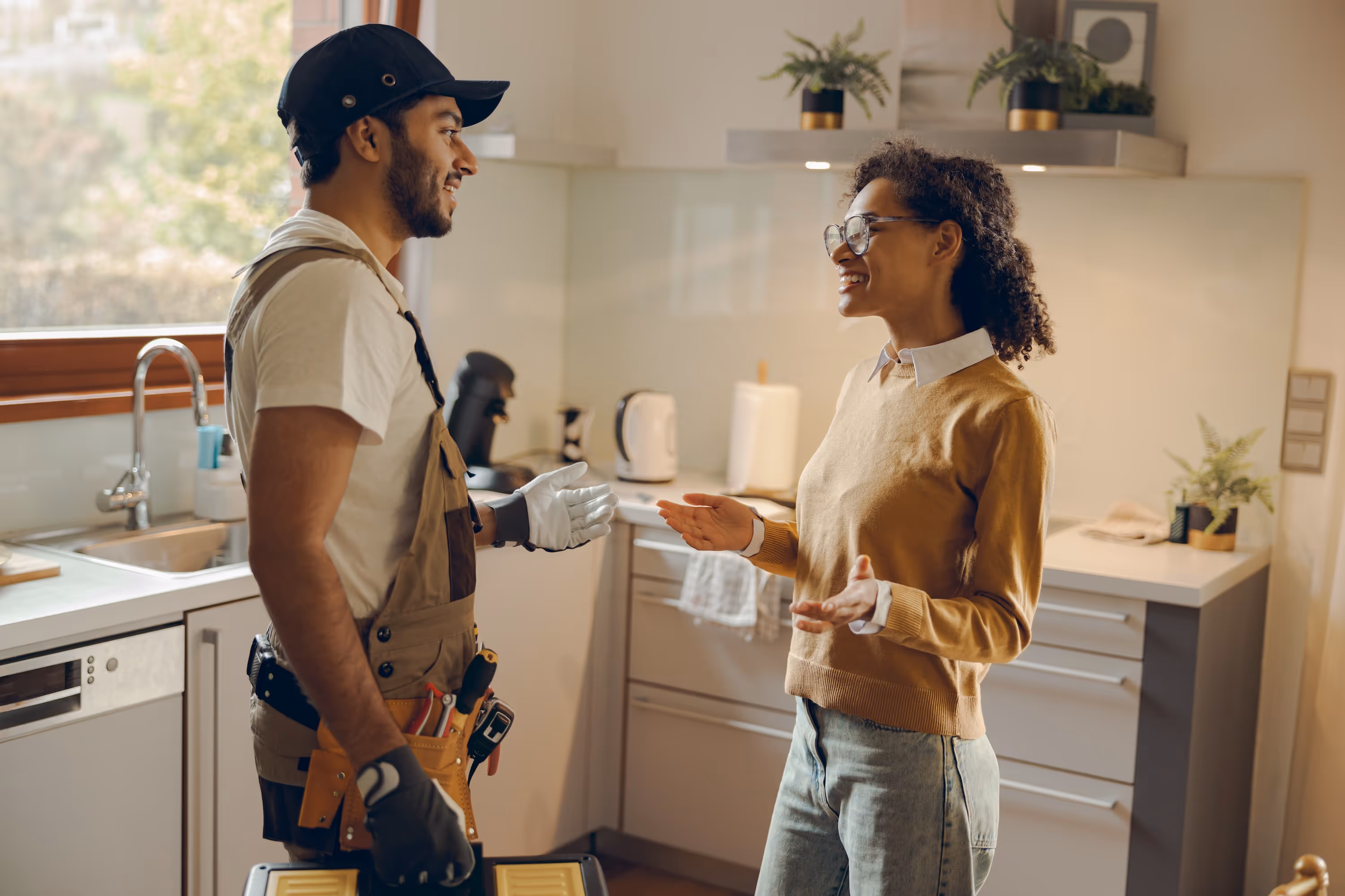 A smiling maintenance technician speaking with a happy resident in her modern apartment kitchen, representing the excellent, responsive service at Enclave at Medina in Von Ormy, TX.