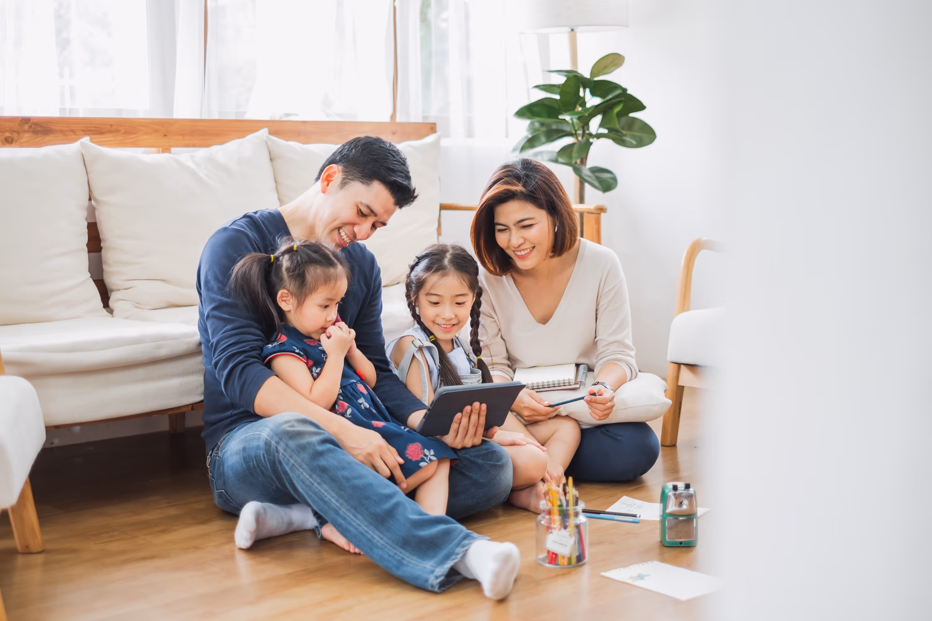 Two adults and two children sitting on a wooden floor looking at a tablet together in their home at Enclave at Medina.