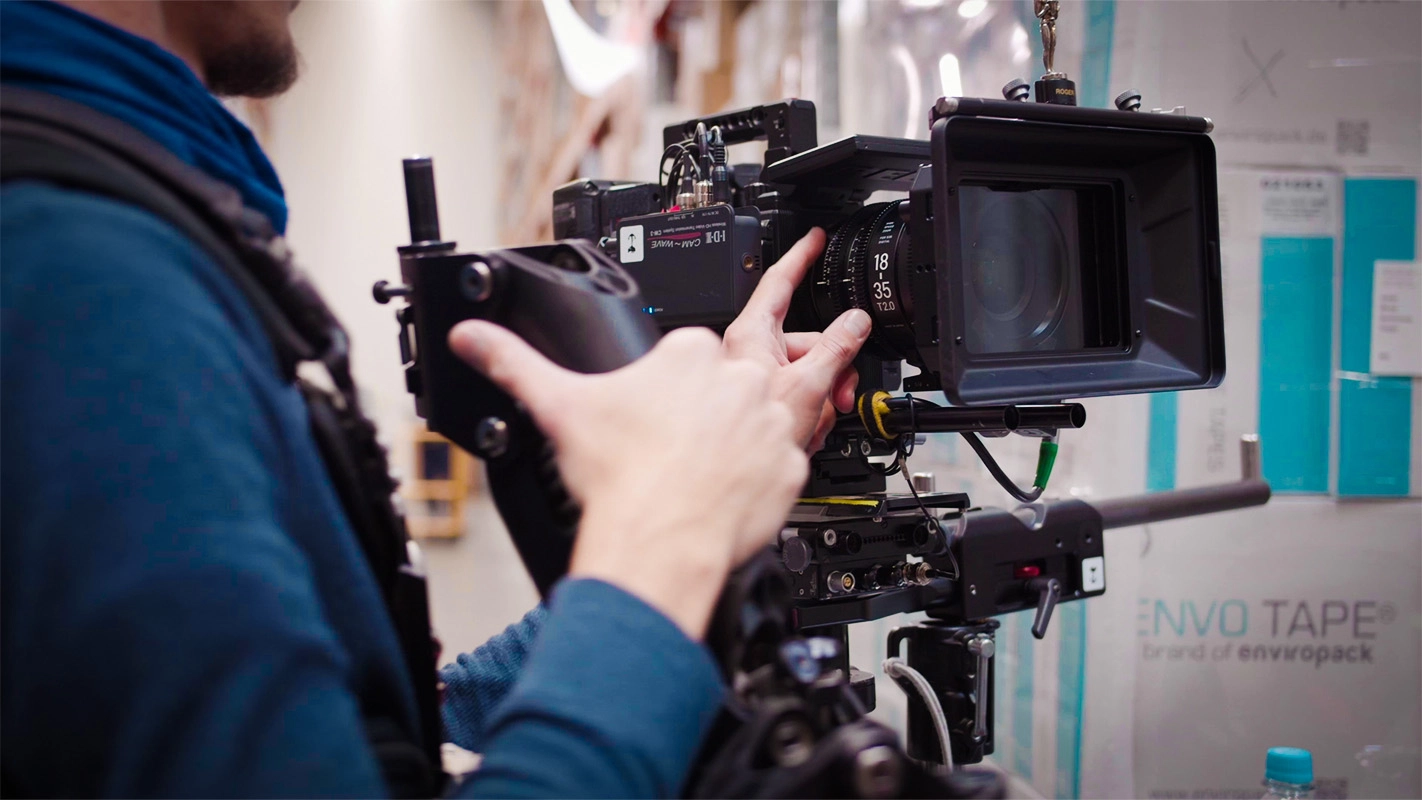 Recruitingfilm der Filmproduktion Panda Pictures aus München und Ulm für Reviderm. Hände eines Kameramanns justieren das Objektiv der Filmkamera am Set.