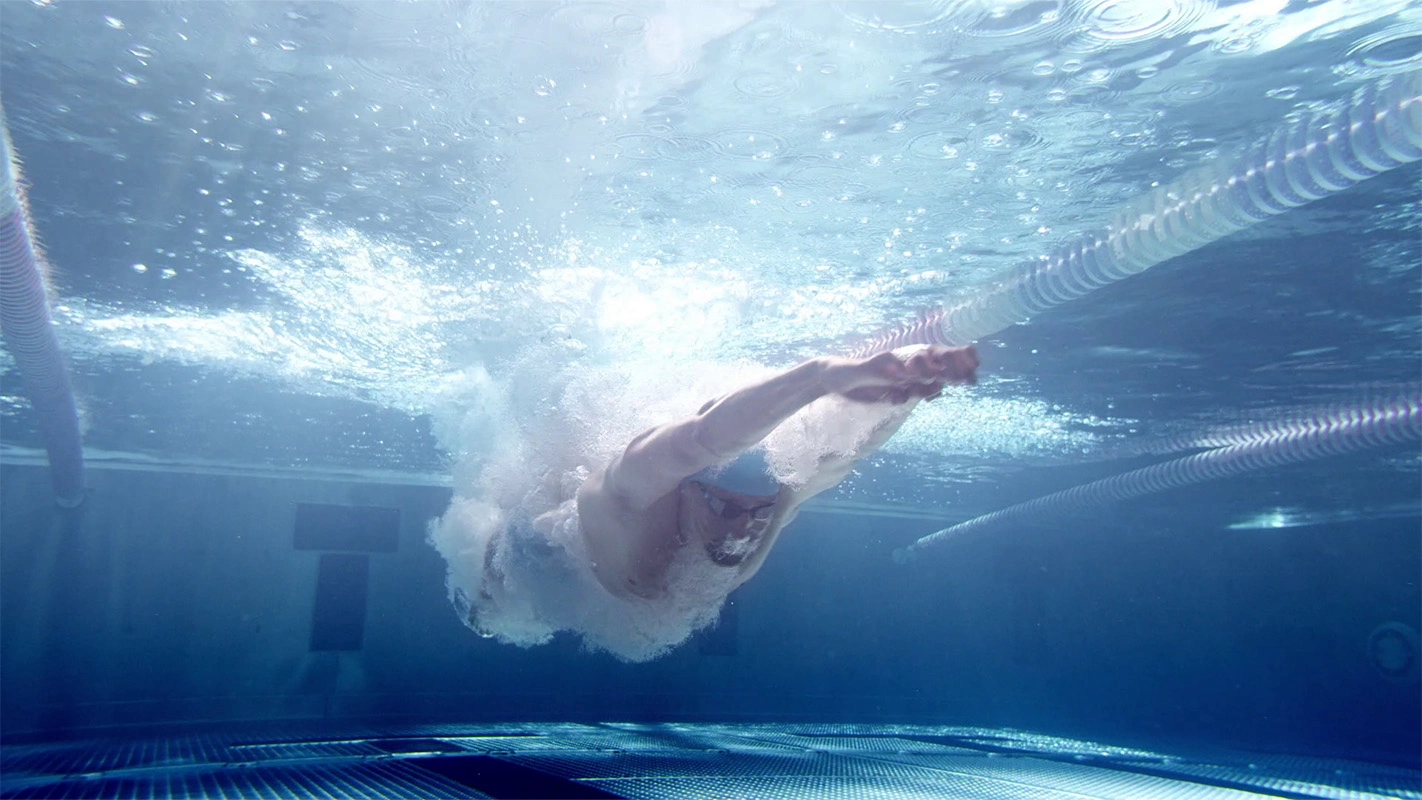 Imagefilm der Filmproduktion Panda Pictures aus München und Ulm für Speedo. Ein Schwimmer stößt sich kraftvoll vom Beckenrand unter Wasser ab, umgeben von aufsteigenden Blasen; eine dramatische Aufnahme, die den Beginn einer Wettkampfszene zeigt.