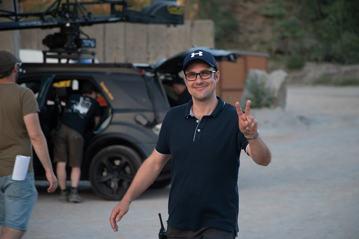 Imagefilm der Filmproduktion Panda Pictures aus München und Ulm für Maxikraft. Ein freundlicher Executive Producer lächelt und zeigt das Victory-Zeichen in die Kamera, umgeben von Teammitgliedern und dem Set.