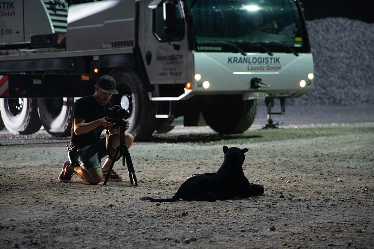 Imagefilm der Filmproduktion Panda Pictures aus München und Ulm für Maxikraft. Ein Kameramann positioniert eine Kamera auf einem Stativ vor einem Lastwagen und einem stehenden Panther-Modell für eine nächtliche Aufnahme.