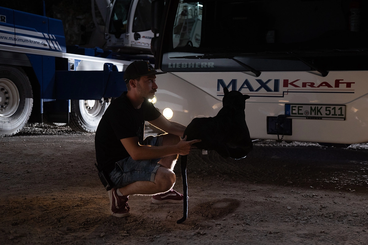 Imagefilm der Filmproduktion Panda Pictures aus München und Ulm für Maxikraft. Ein Darsteller kniet neben einem Panther-Modell auf dem Boden, während im Hintergrund ein LKW von Maxikraft für die Szene positioniert ist.