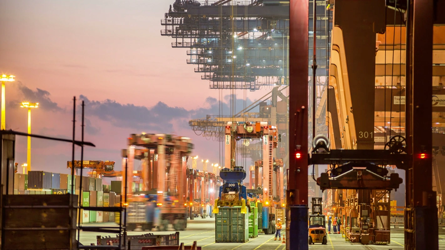Imagefilm der Filmproduktion Panda Pictures aus München und Ulm für SupplyOn. Containerkräne und Lastwagen im geschäftigen Hafen bei Sonnenuntergang, eingefangen mit cinematicer Farbgebung und Komposition.