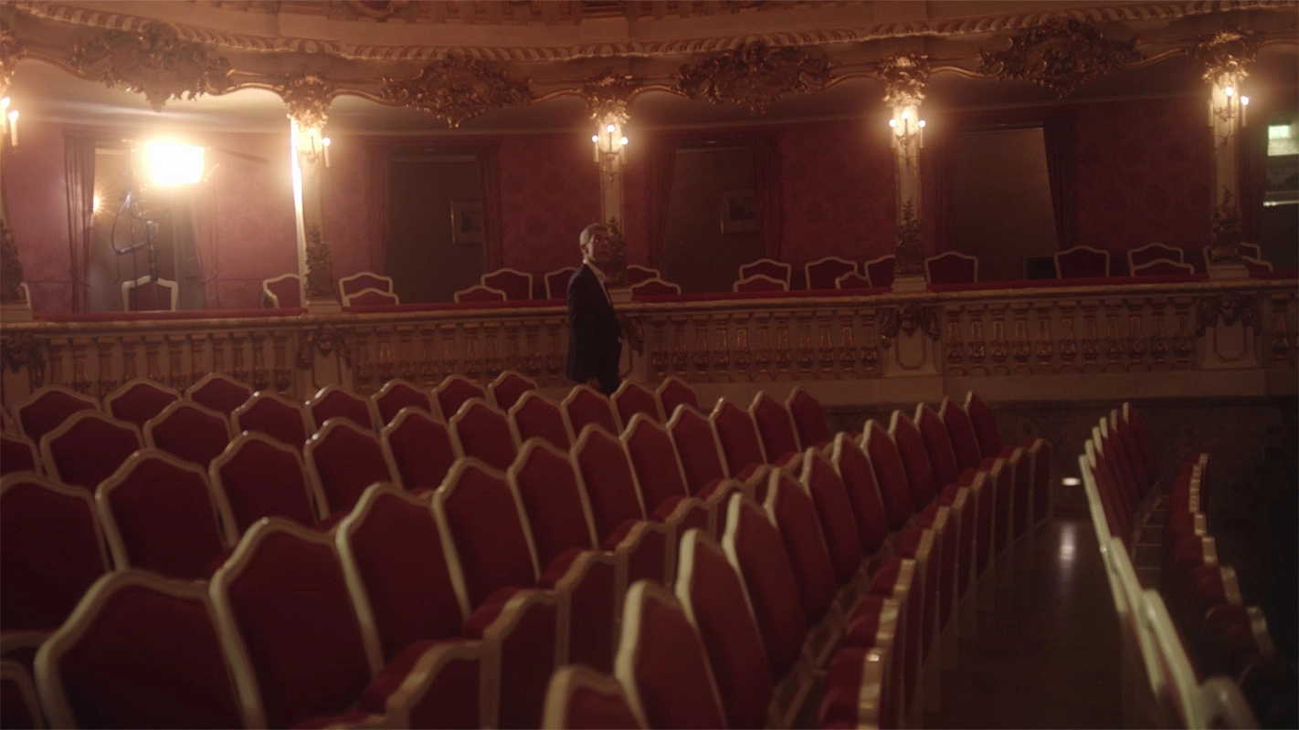 Weihnachtsfilm der Filmproduktion Panda Pictures aus München und Ulm für UniCredit. Der Protagonist geht durch die Reihen eines roten Theatersaals, eine Inszenierung, die seine Präsenz im opulenten Ambiente betont.