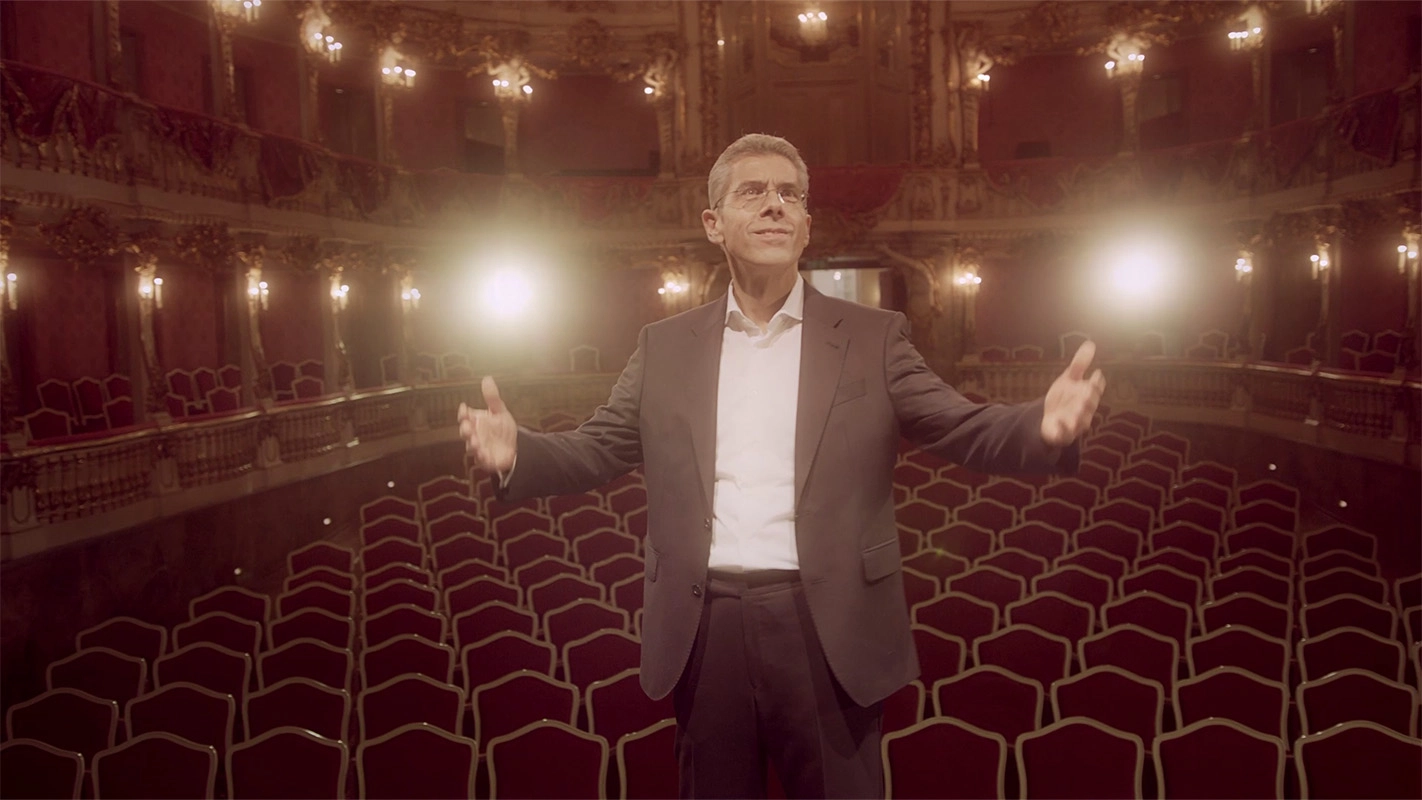 Weihnachtsfilm der Filmproduktion Panda Pictures aus München und Ulm für UniCredit. Der Protagonist mit ausgebreiteten Armen im leeren Theatersaal, eine Geste, die Offenheit und Präsentation des Raumes ausdrückt.