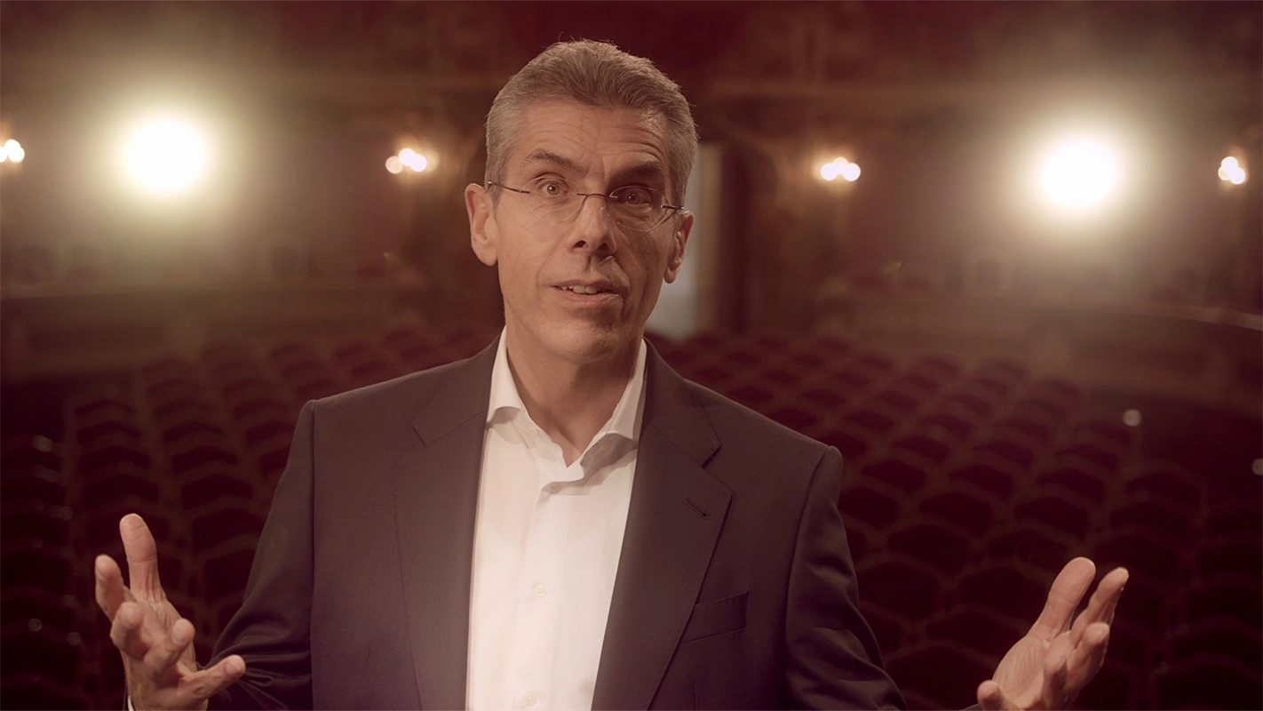 Weihnachtsfilm der Filmproduktion Panda Pictures aus München und Ulm für UniCredit. Der Protagonist blickt direkt in die Kamera mit offen ausgebreiteten Armen, eine einladende Geste vor der Theaterkulisse.
