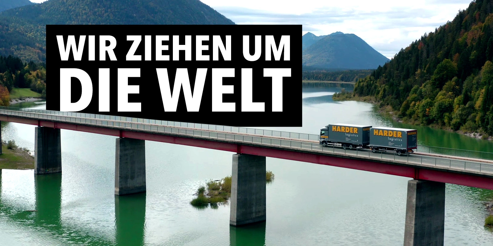 Imagefilm der Filmproduktion Panda Pictures aus München und Ulm für HARDER. Ein Harder-Lkw fährt über eine Brücke über einen See, mit Bergen im Hintergrund. Der Text "WIR ZIEHEN UM DIE WELT" ist im Vordergrund platziert. Einprägsamer Filmtitel.