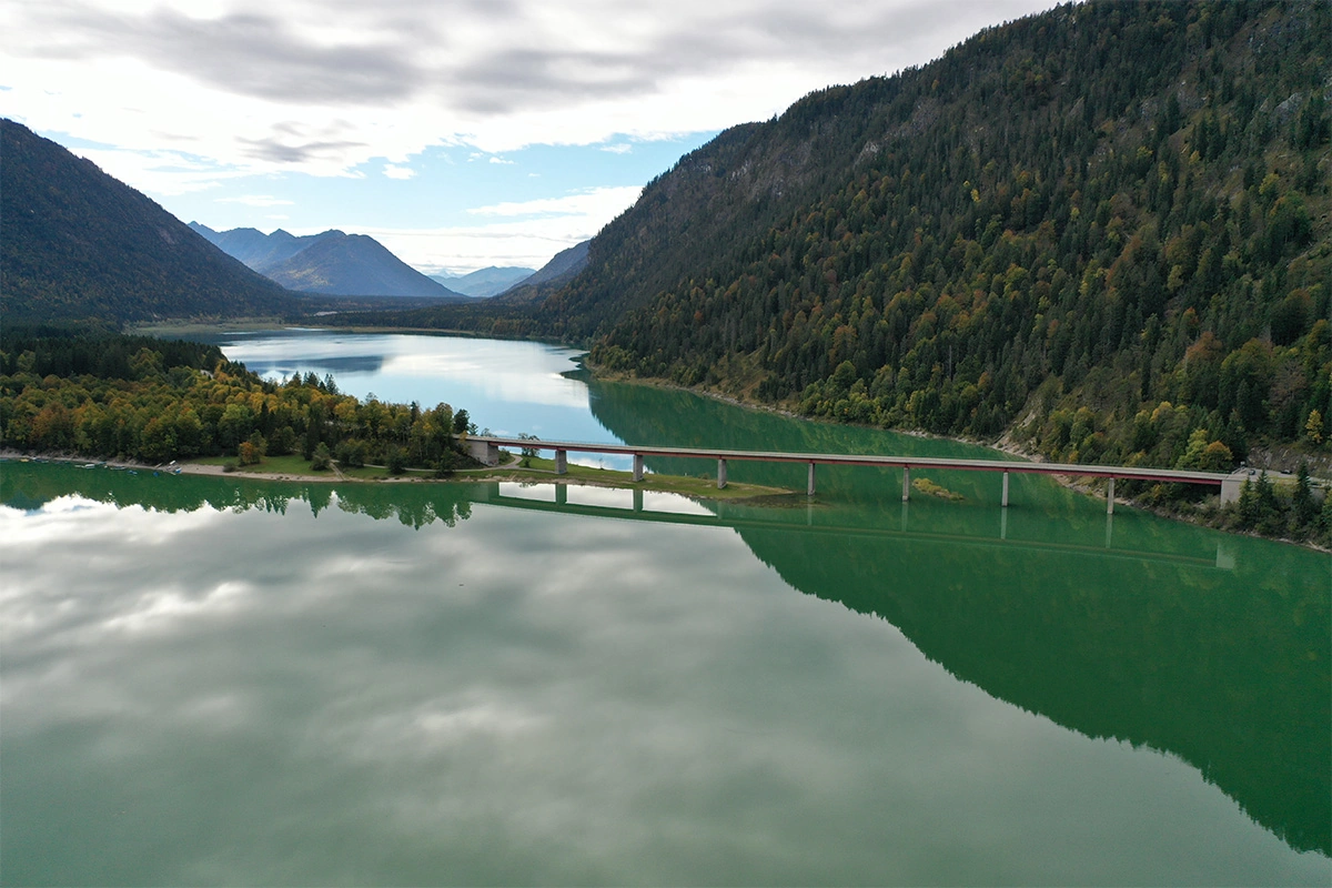 Imagefilm der Filmproduktion Panda Pictures aus München und Ulm für HARDER. Ein tiefgrüner See inmitten einer malerischen Berglandschaft, dazwischen eine ikonische Brücke. Perfekte Kulisse für Fahraufnahmen.