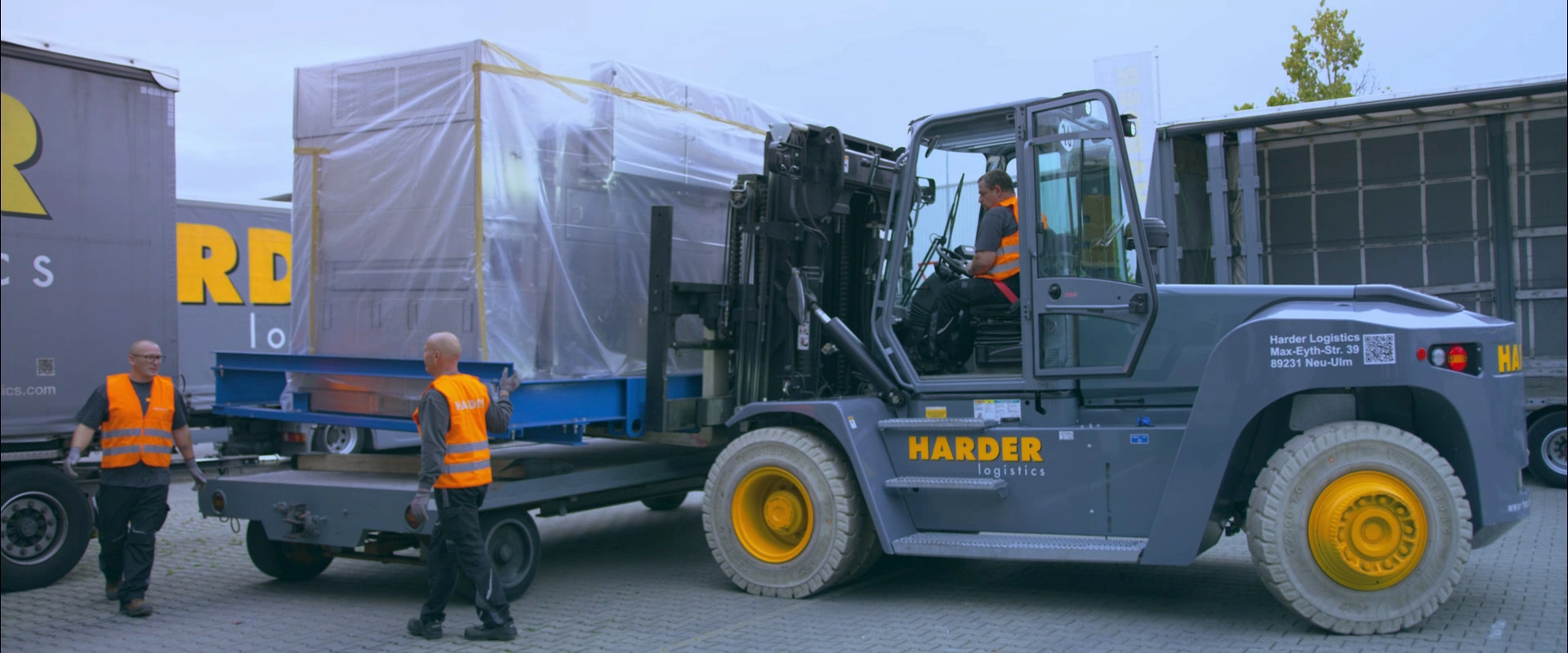 Imagefilm der Filmproduktion Panda Pictures aus München und Ulm für HARDER. Ein Gabelstapler verlädt ein großes, verpacktes Objekt auf einen Lkw, assistiert von zwei Logistikern. Eine detaillierte Momentaufnahme des Arbeitsablaufs.